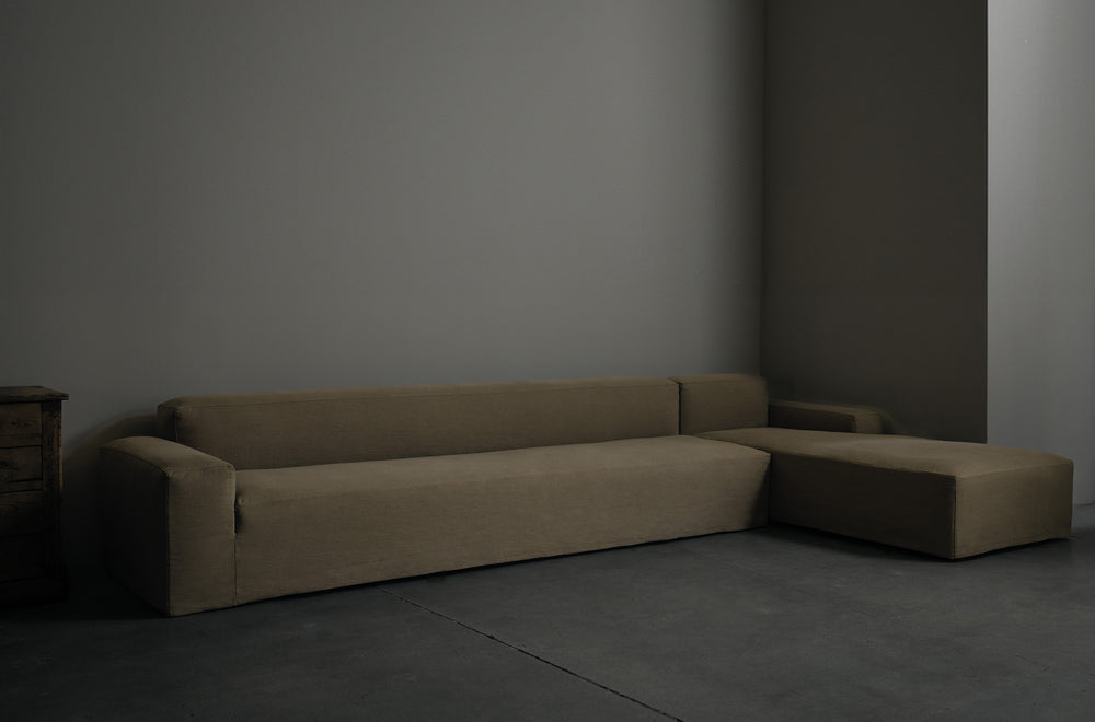 A large upholstered velvet sectional with a modern, minimal design in a tan velvet fabric displayed against a neutral background