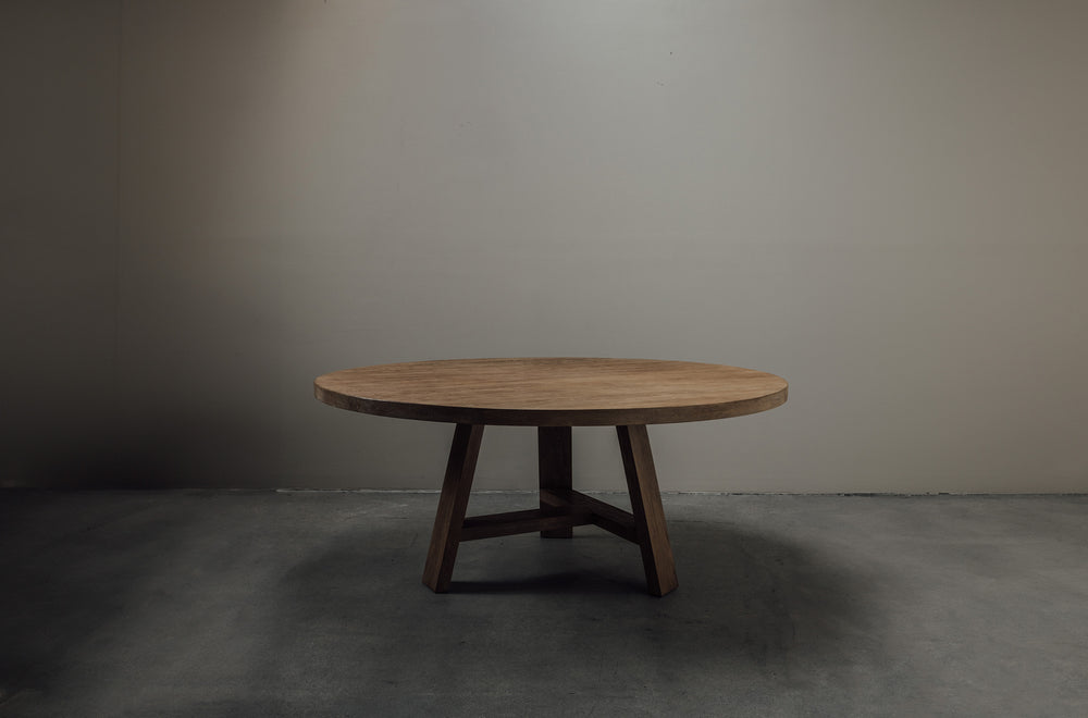 A round wooden table with three legs, placed against a plain background.